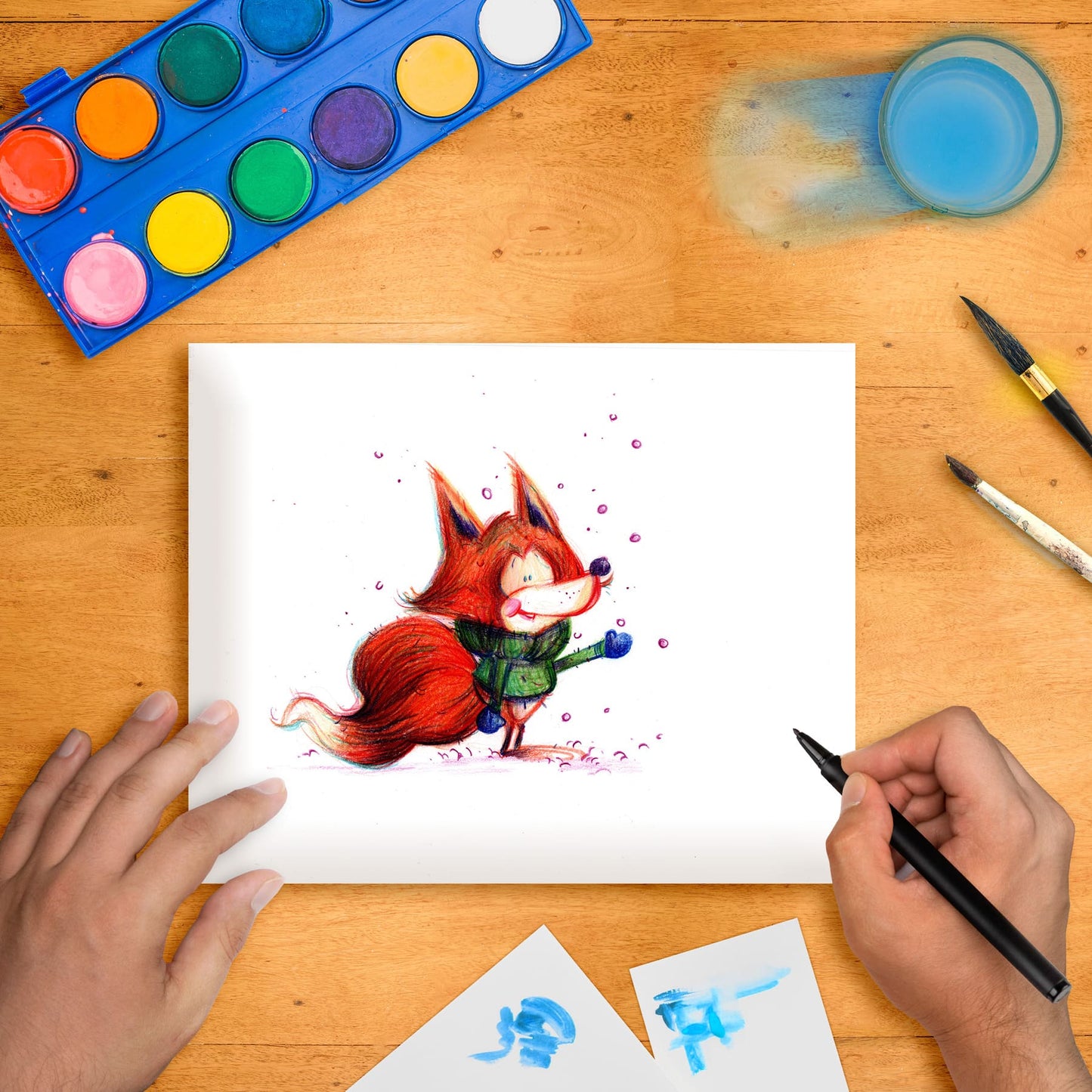 Original marker illustration of a winter fox on a table with art supplies around it, including a palette of colors, brushes, and another piece of paper with a blue drawing.