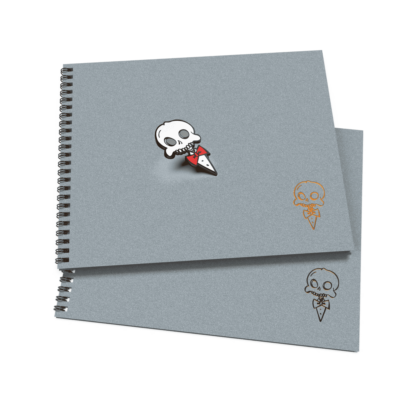 Two gray sketchbooks with a wire-o binding, one featuring a small, stylized skull and crossbones enamel pin on the cover.