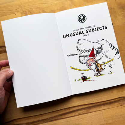 Open Anthony Wheeler’s Unusual Subjects Vol. 2 book showing a gnome investigator and dinosaur illustration on a wooden tabletop.