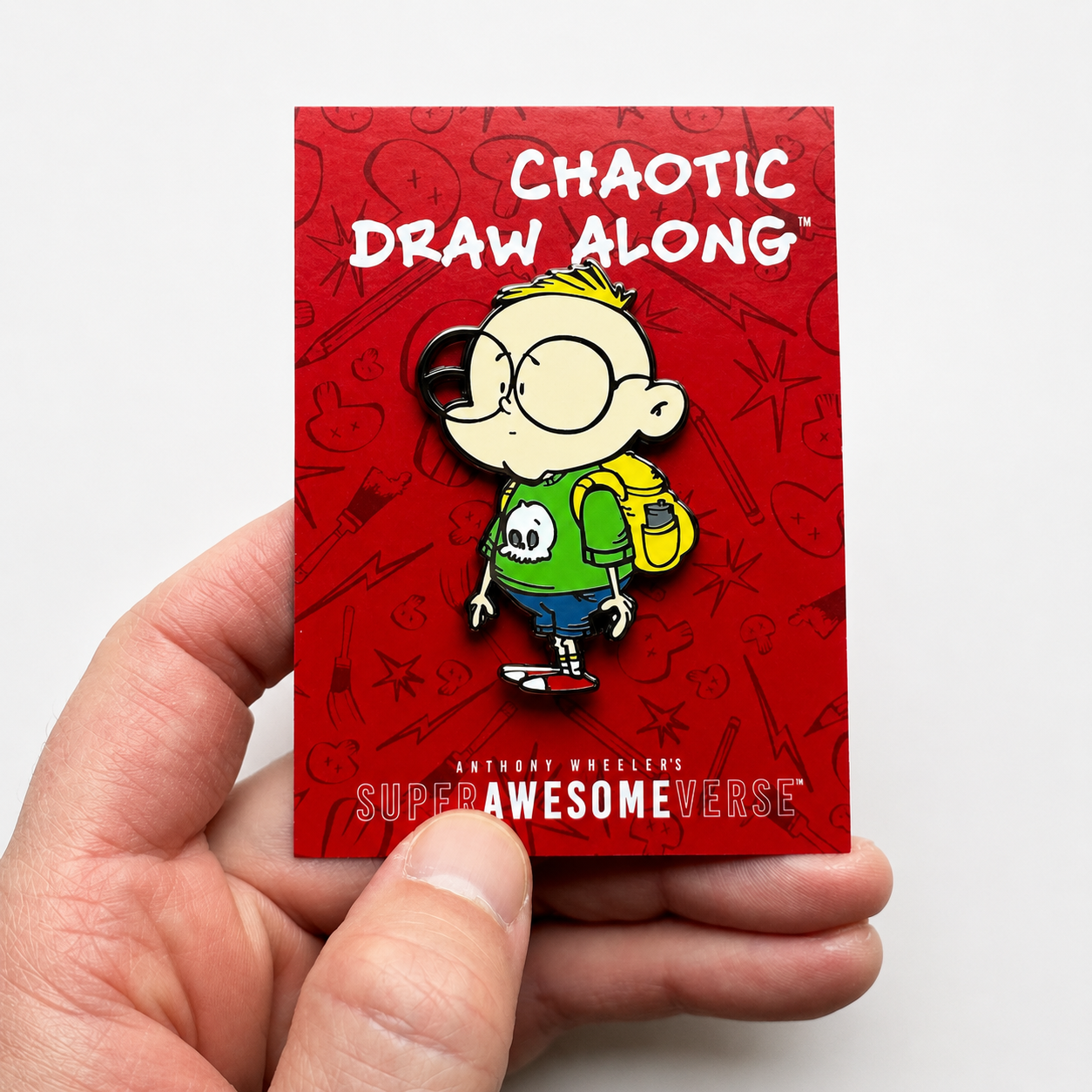 Hand holding the Chaotic Draw Along enamel pin on its red branded backing card.