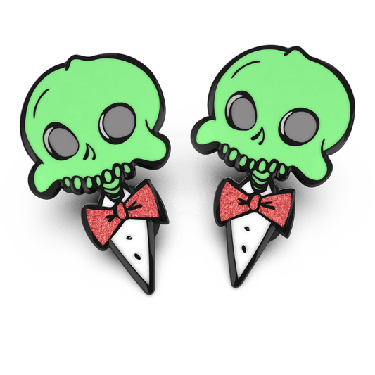 Two enamel pins with a glow in the dark effect, featuring a character with a skeleton grin and a red bow tie.