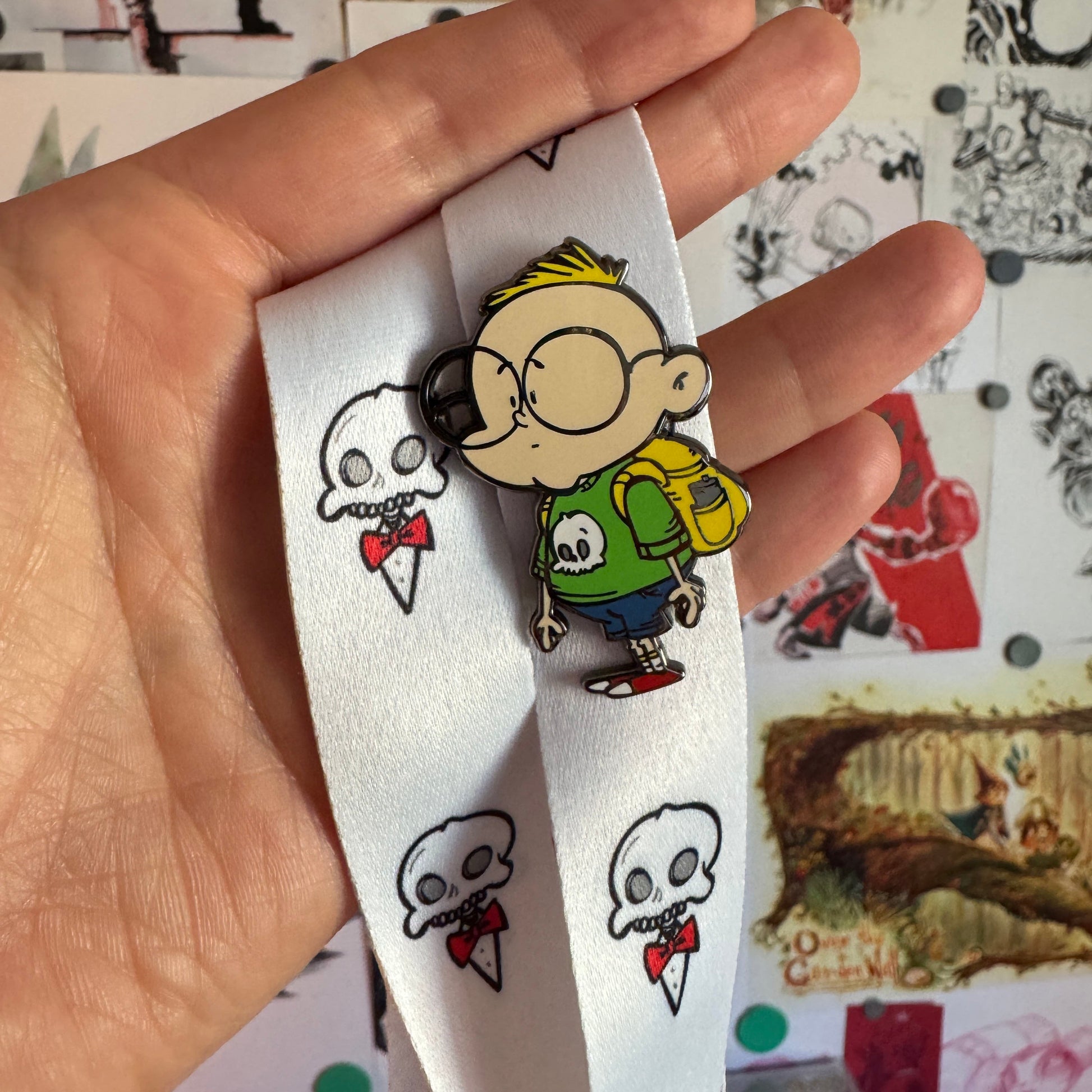 Gil hard enamel pin displayed on the Skelly lanyard featuring white fabric with repeating skull and red bow tie illustrations.