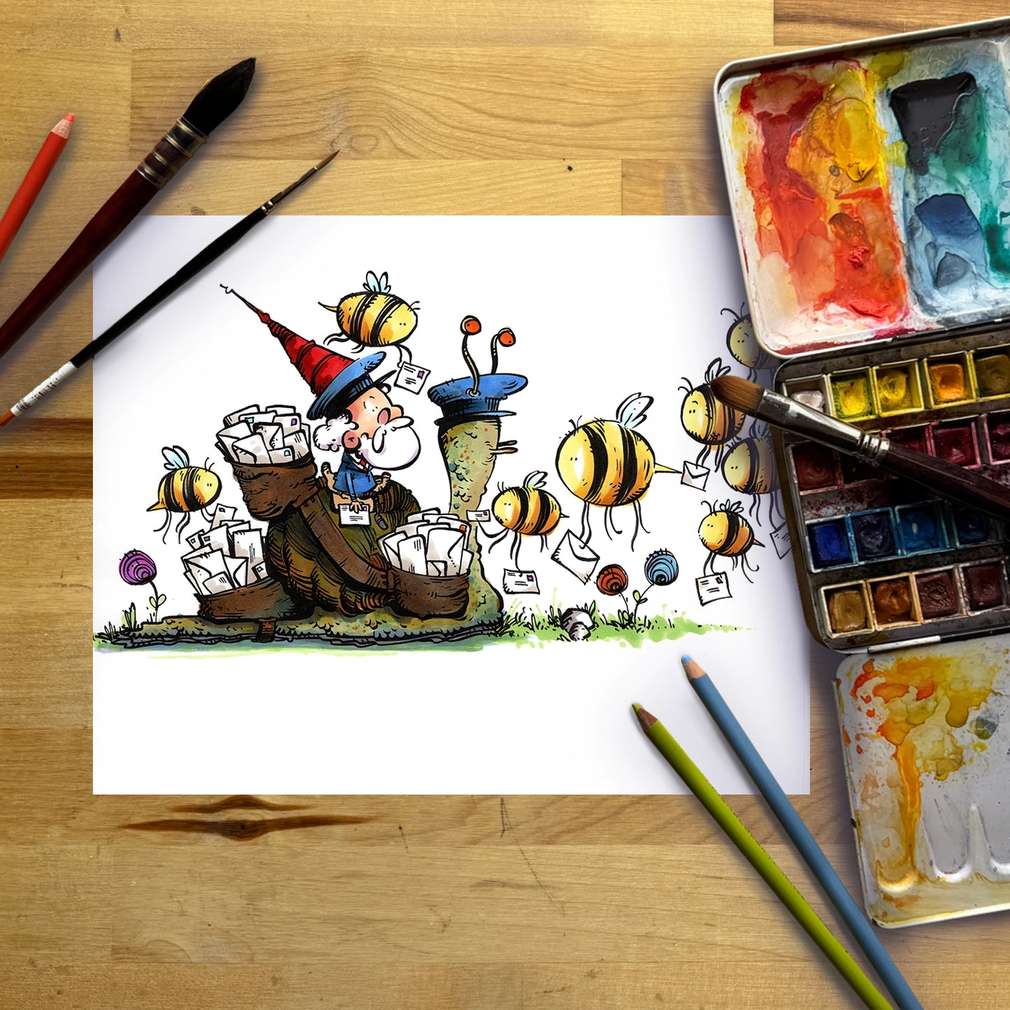A hand-drawn cartoon illustration of a wizard surrounded by bees, shown on a sheet of white paper laid flat on a wooden table with paintbrushes, watercolor paints, and colored pencils.