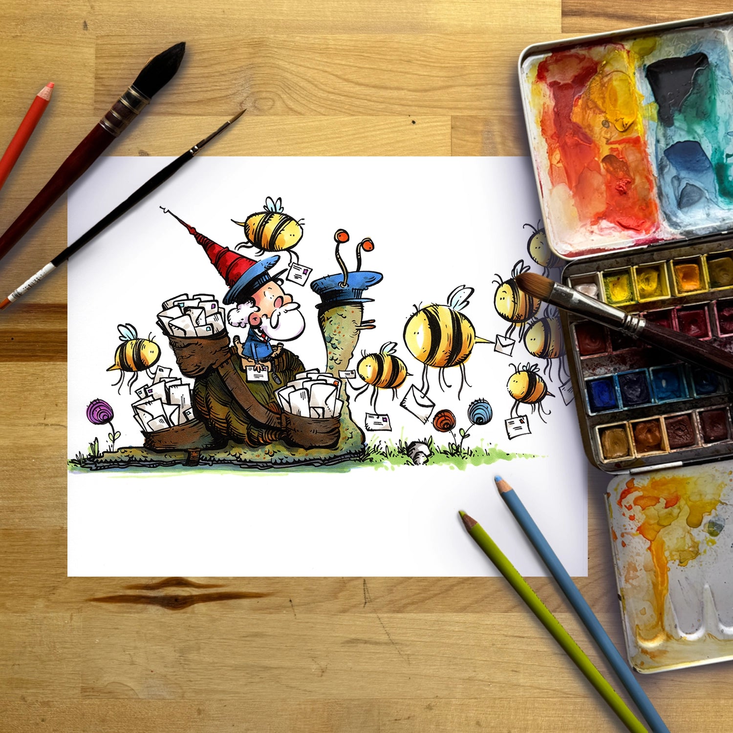 A hand-drawn cartoon illustration of a wizard surrounded by bees, shown on a sheet of white paper laid flat on a wooden table with paintbrushes, watercolor paints, and colored pencils.