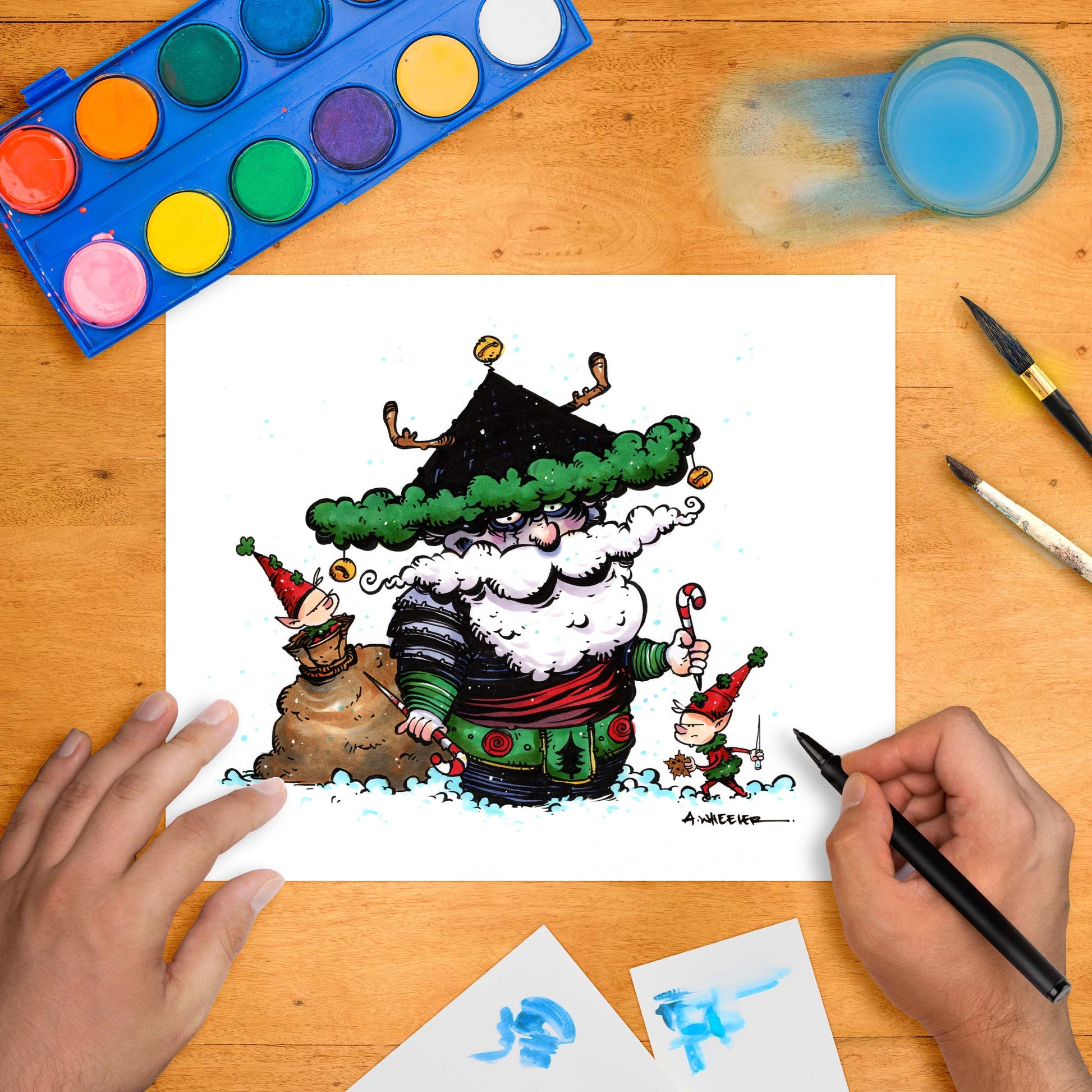 Festive artwork of a stylized Santa dressed as a samurai warrior, flanked by mischievous elves, with drawing tools and a paint palette arranged around the hand-colored print on a wooden desk.