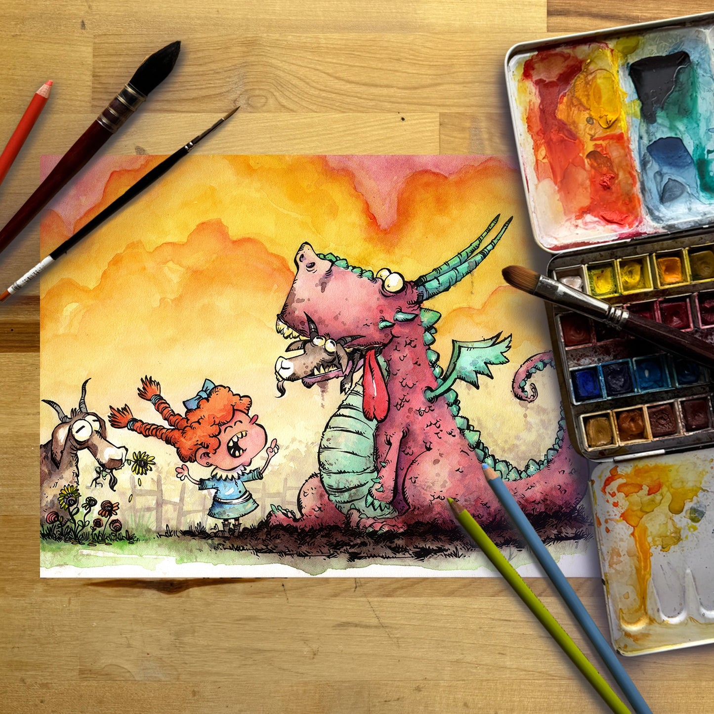 A colorful watercolor painting of a pink dragon and a red-haired girl on a wooden table, surrounded by paintbrushes, a watercolor palette, and two pencils.