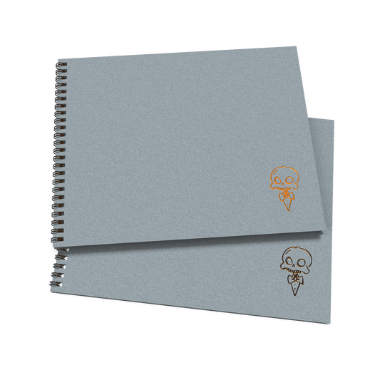 A stack of two gray sketchbooks with a decorative skull and crossbones design on the cover.